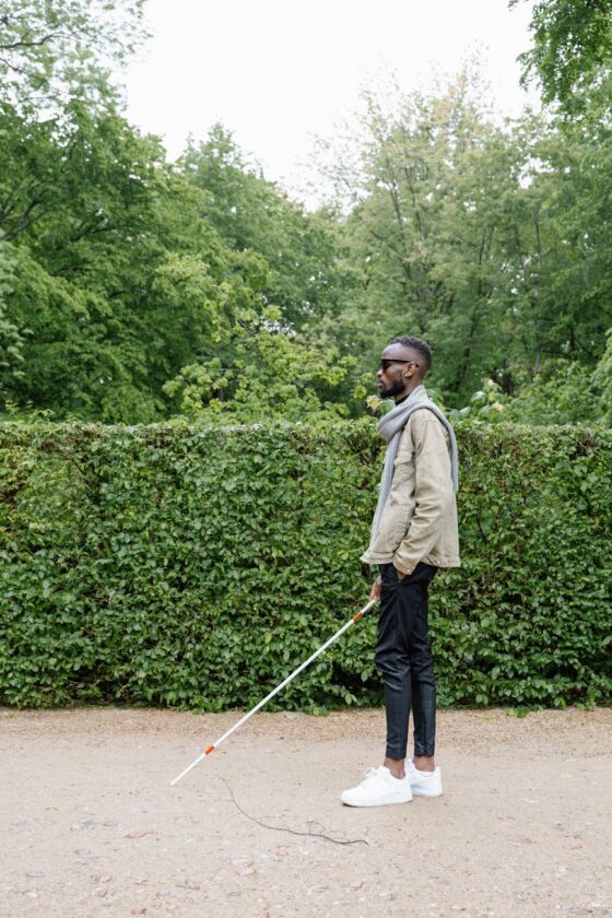 man in beige jacket waling with a white cane