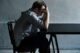 Hombre sentado junto a una mesa con la cabeza apoyada en la mano, en una habitación gris en penumbra
