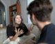 Mujer sentada en un sofá habla gesticulando con las manos frente a un hombre que la escucha de espaldas