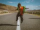Niño pequeño saltando en medio de una carretera, en un paisaje árido y soleado