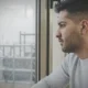 Hombre adulto mira por una ventana mojada por la lluvia, con expresión seria.