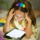Niña sentada a la mesa con las manos en la cabeza mientras mira una tablet